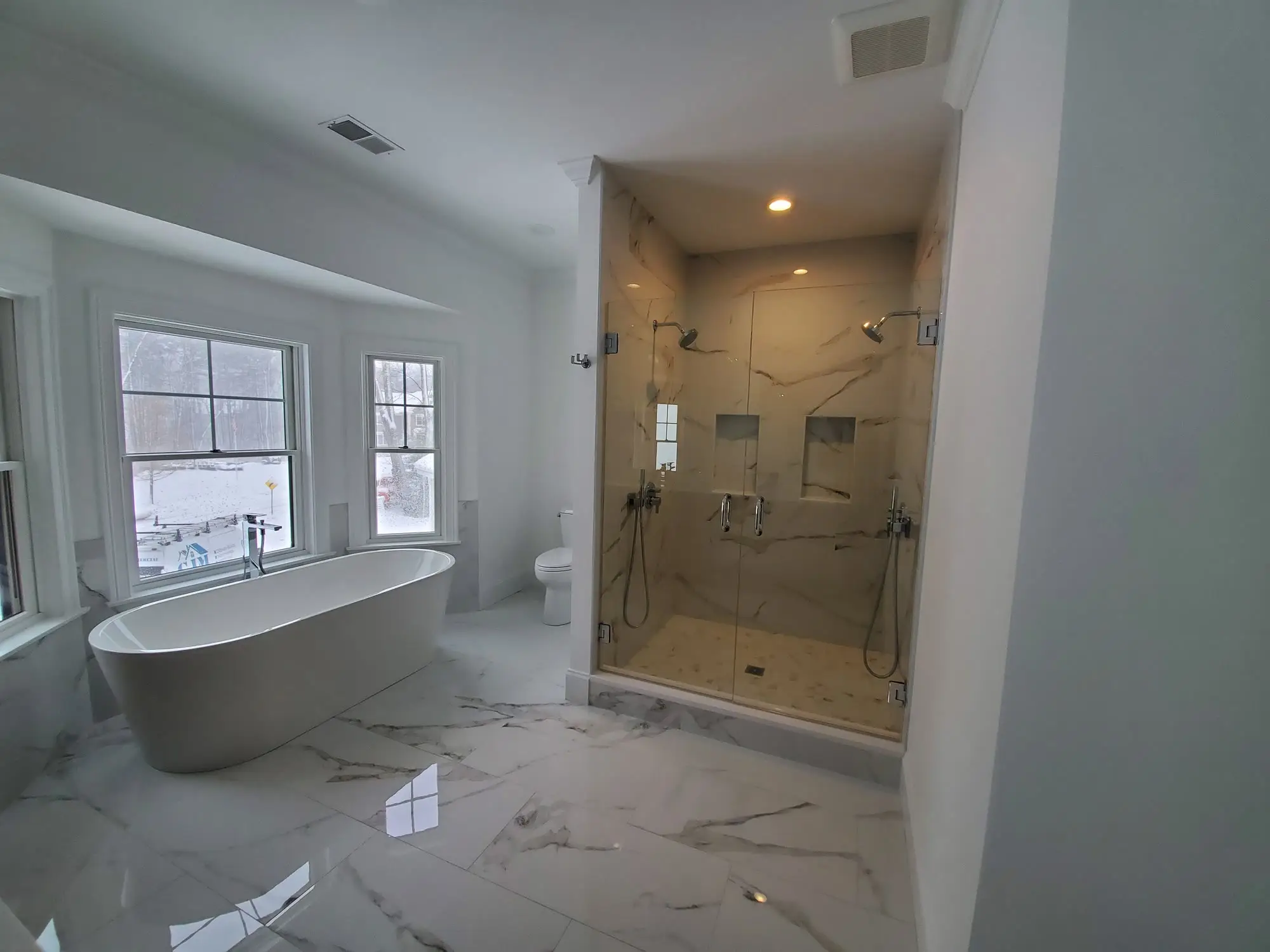 Freestanding tub in a bay window with a glass double shower in marble-look tile, a tiled niche, and large-format marble-look porcelain floors.