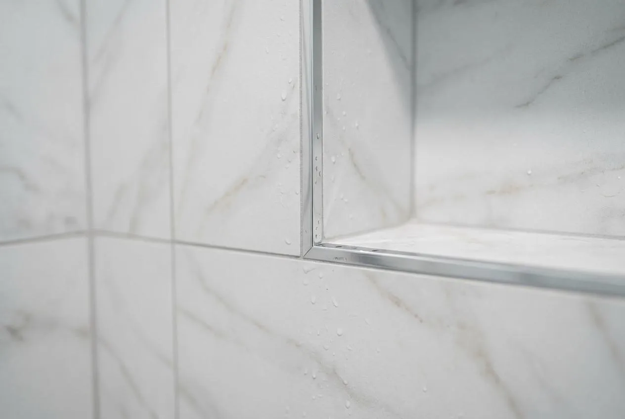 Marble-look porcelain shower tile with a recessed chrome-trimmed niche — one of the shower-wall materials CJM Builders installs