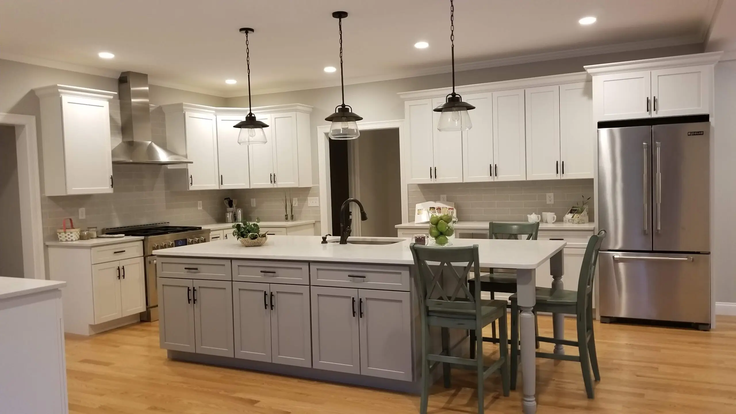 A finished open-concept kitchen remodel by CJM Builders with white shaker cabinetry, a gray island with seating, and pendant lighting