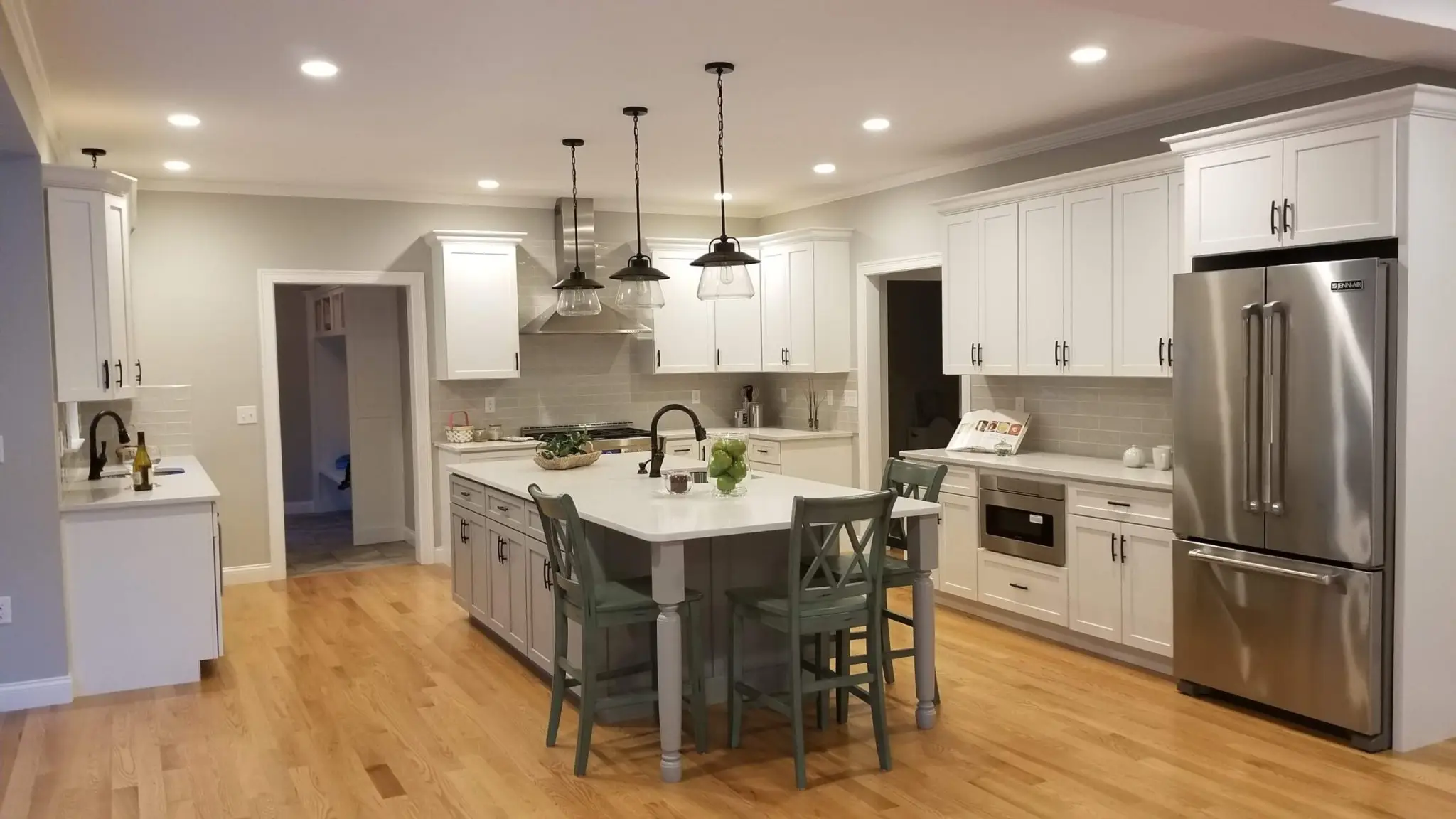 A finished kitchen remodel by CJM Builders with white cabinetry, a gray island with counter stools, stainless appliances, and warm hardwood floors