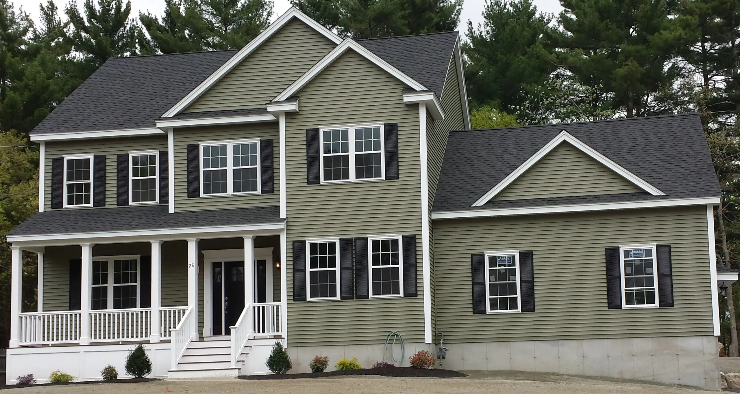 A completed custom home by CJM Builders with sage-green siding, white trim, black shutters, a covered front porch, and an attached two-car garage