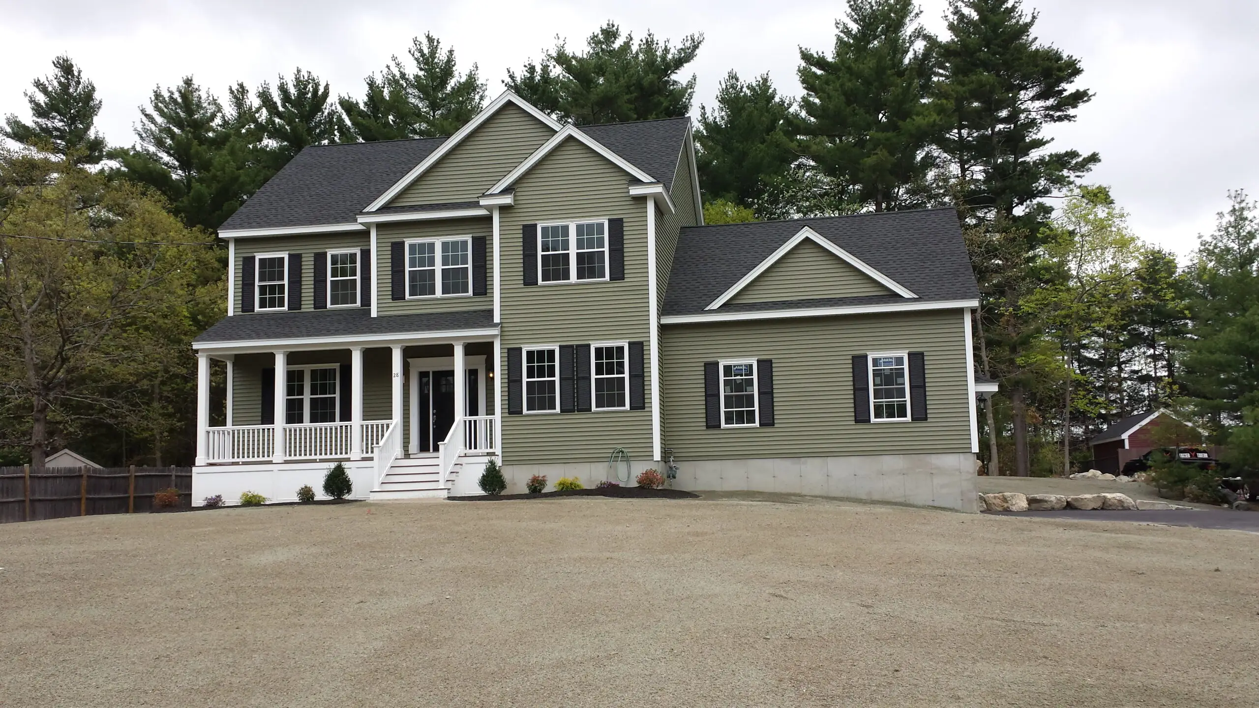 A finished custom home by CJM Builders with sage-green siding, white trim, and an attached two-car garage, set back on a wide wooded lot
