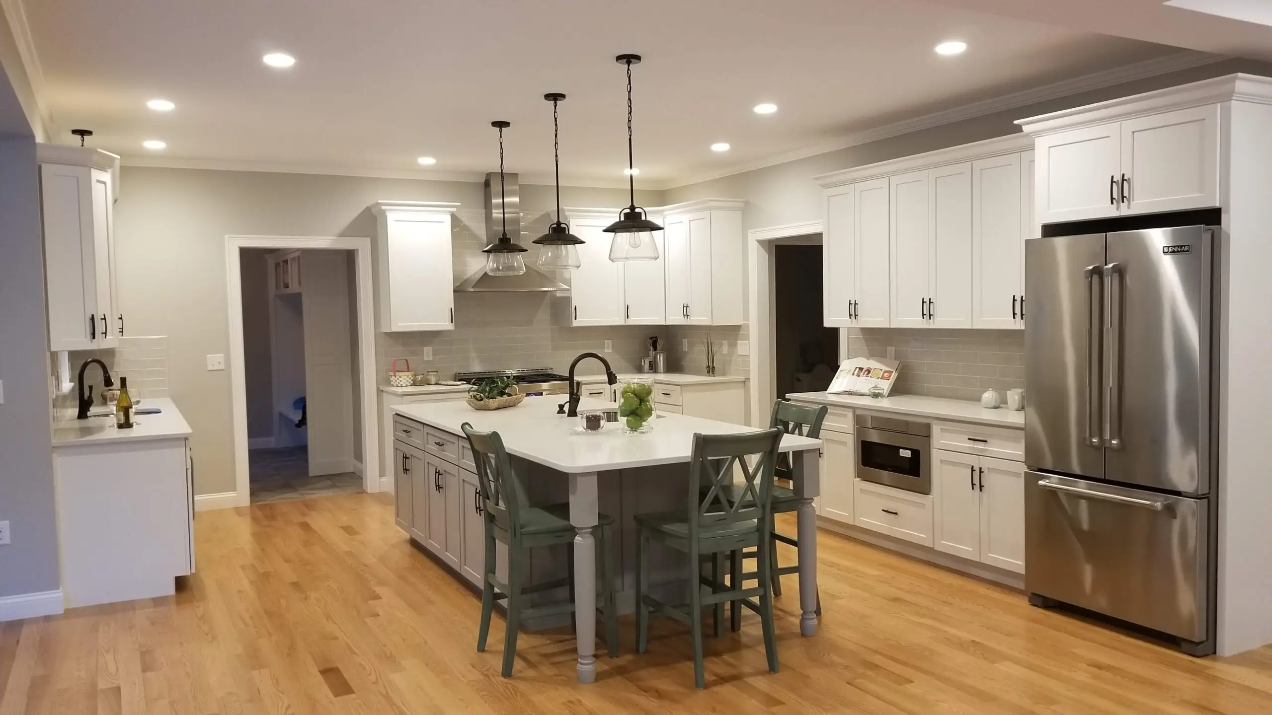 A finished open-concept kitchen remodel by CJM Builders with white shaker cabinetry, a blue-gray island with counter seating, stainless appliances, and hardwood floors