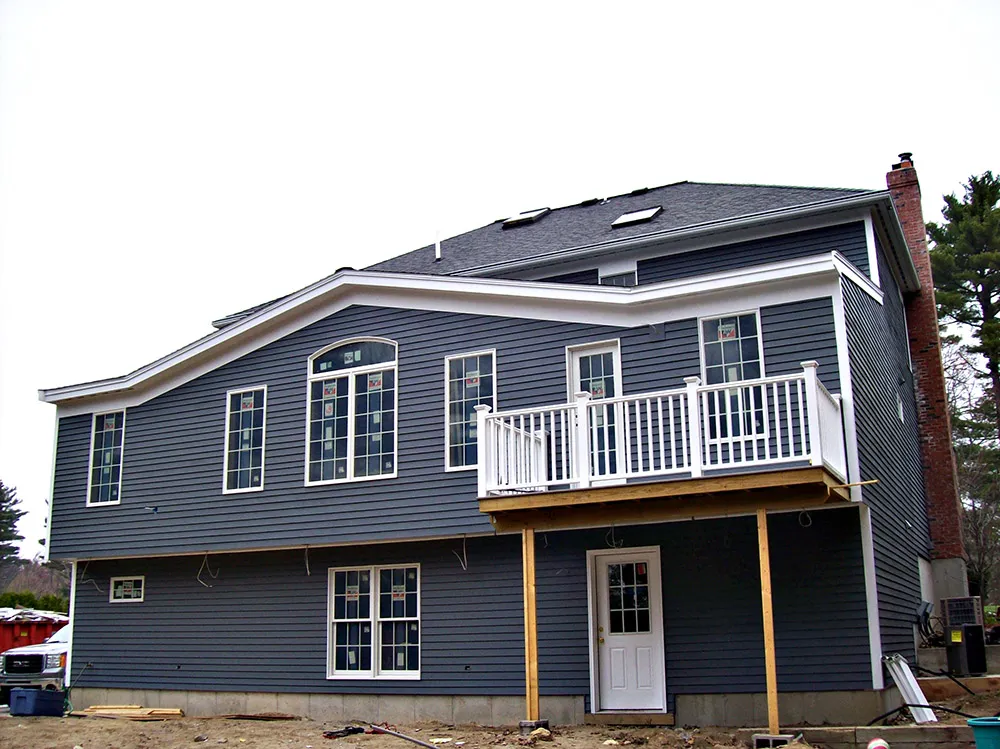 A new blue-gray home under construction by CJM Builders, with siding and a second-floor balcony going on