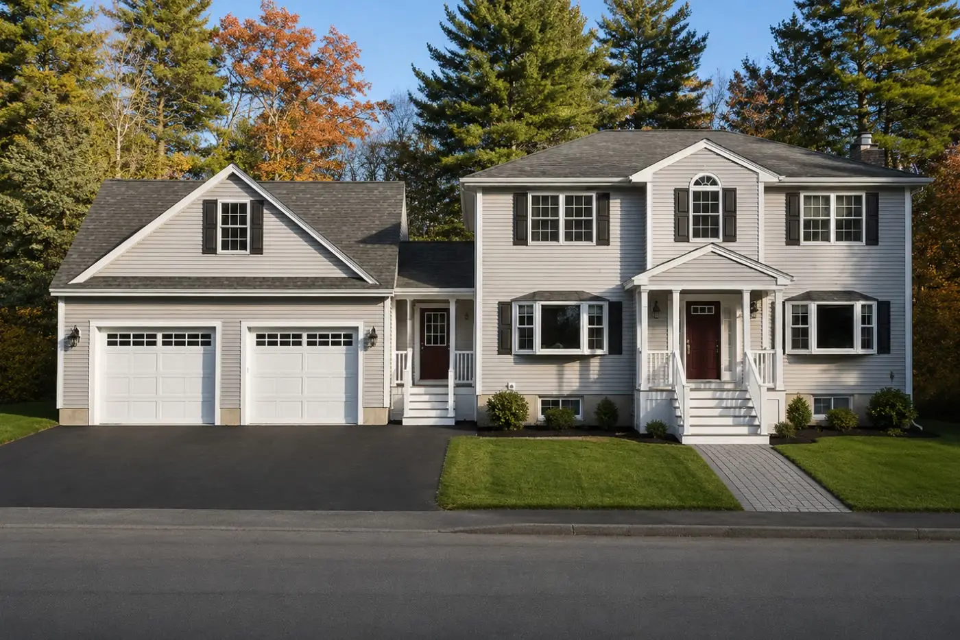 Cream two-story home with a new attached two-car garage wing and dormer on the left, in autumn