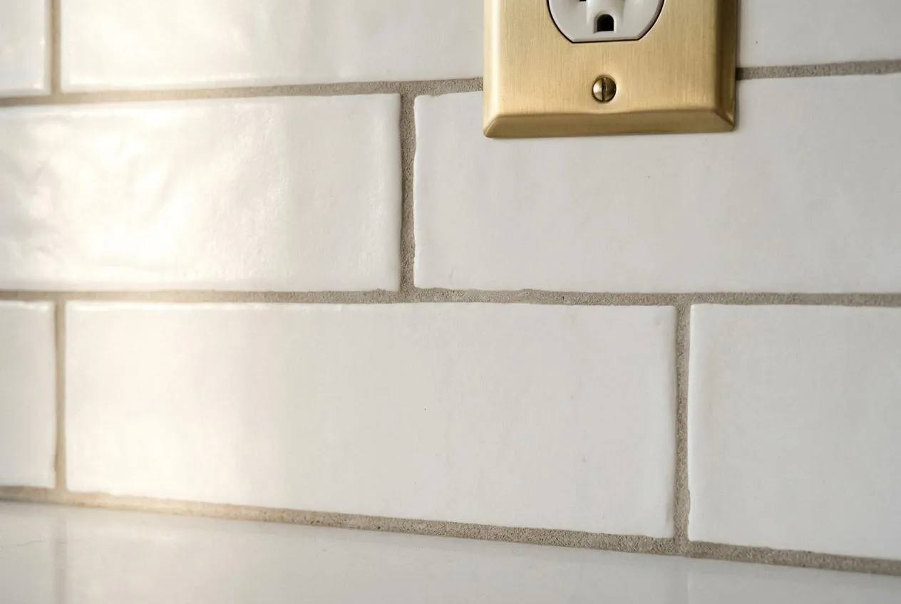 White subway tile backsplash with warm grout and brass outlet cover — material detail