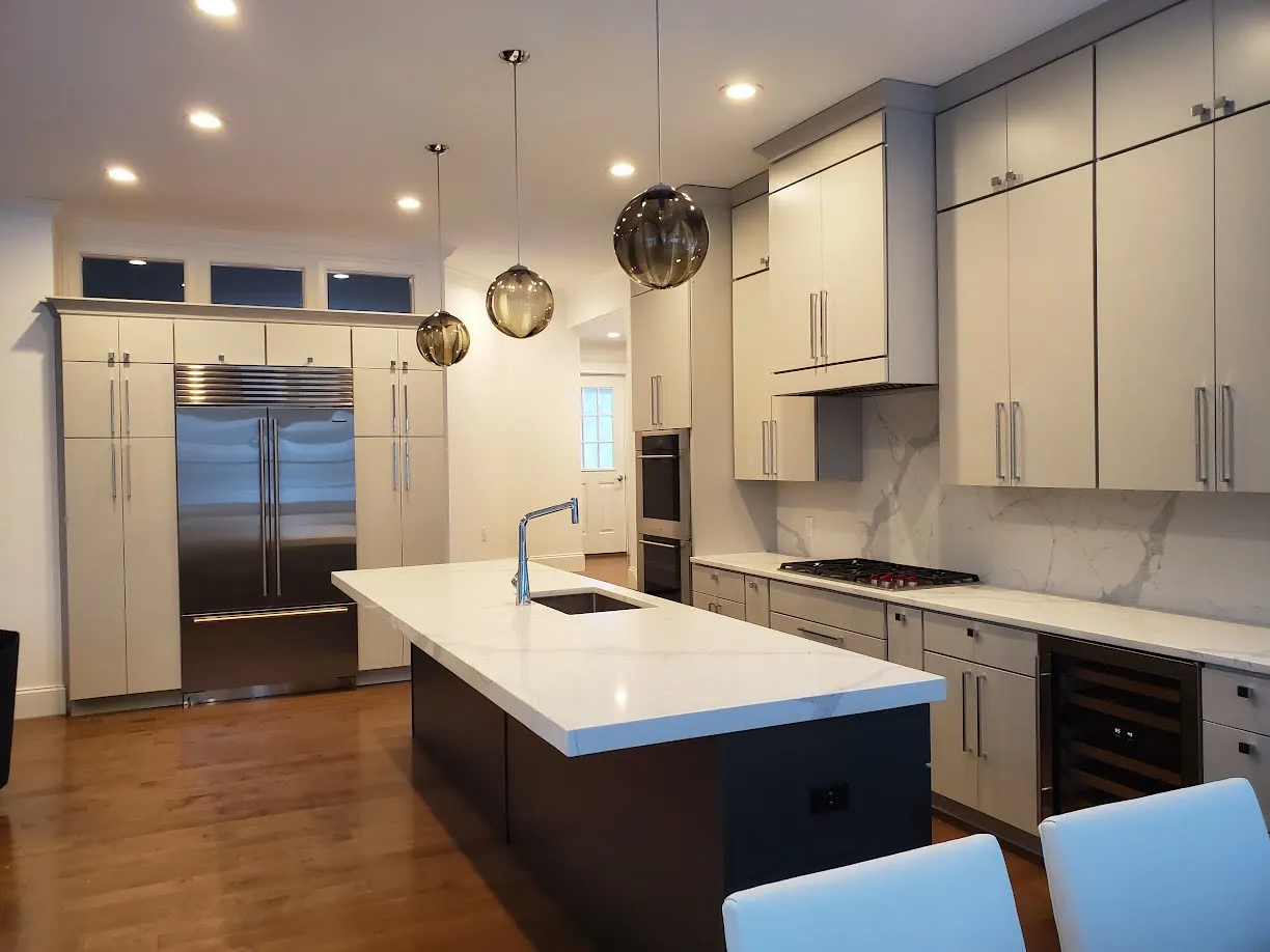 Modern kitchen with light gray slab cabinets, a built-in stainless refrigerator, a black island with white quartz top, bronze glass pendants, and transom windows
