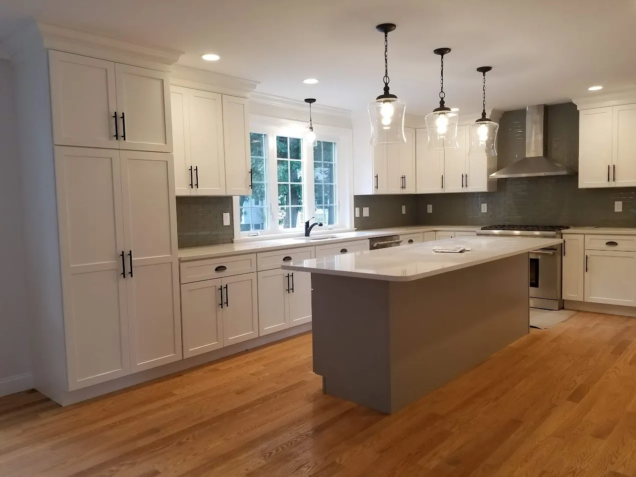 White shaker kitchen with a wall of tall pantry cabinets, a taupe island with white top, gray glass subway backsplash, and three glass pendants