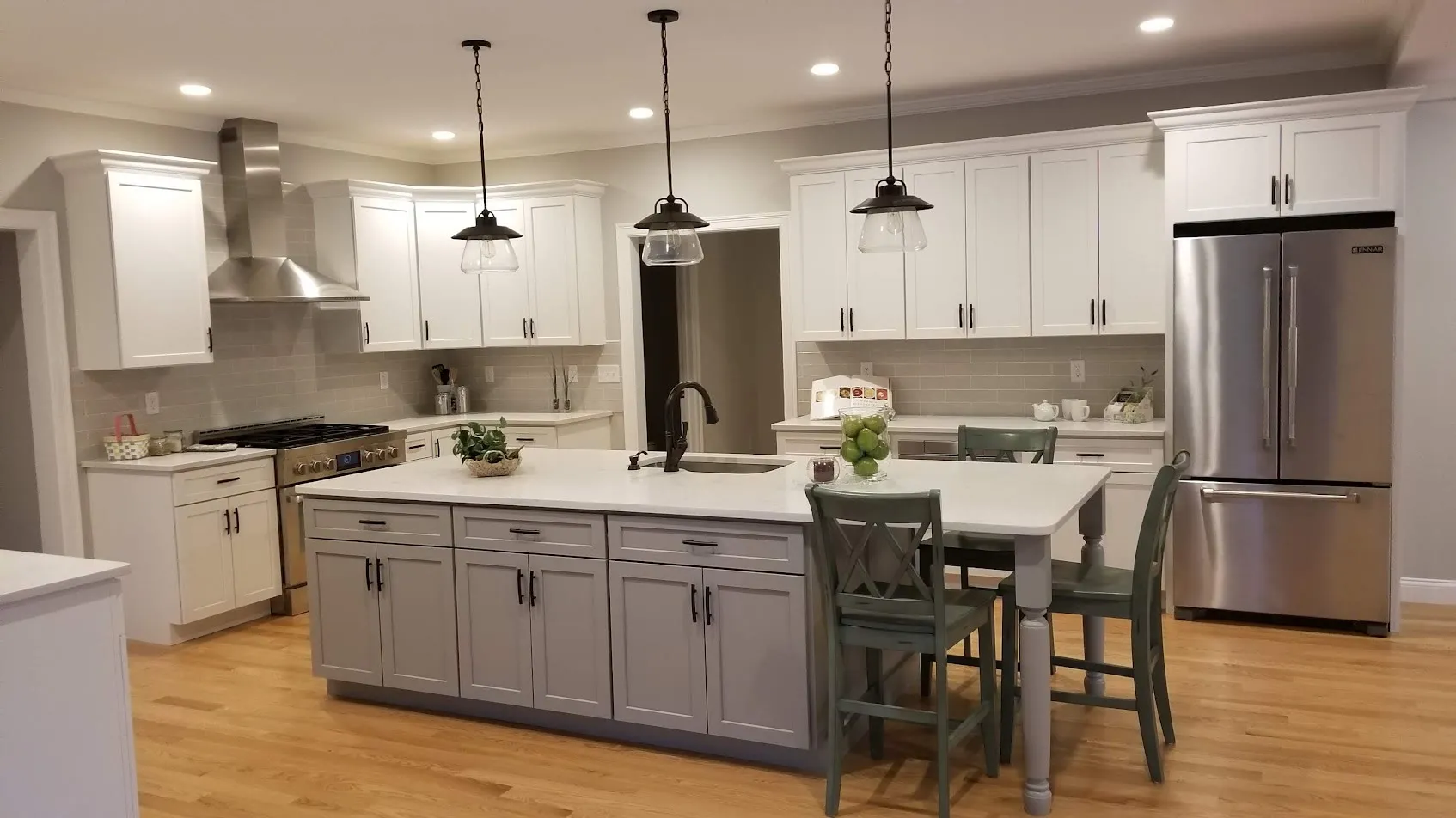 White shaker kitchen with a gray island, white quartz top, sage farmhouse dining chairs, black pendants, and a stainless French-door refrigerator on light hardwood