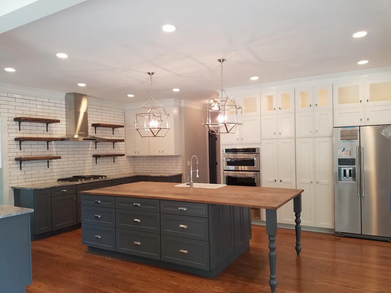 White shaker kitchen with a navy island topped in butcher block, white subway tile, open wood shelves, brass cage pendants, and a stainless refrigerator