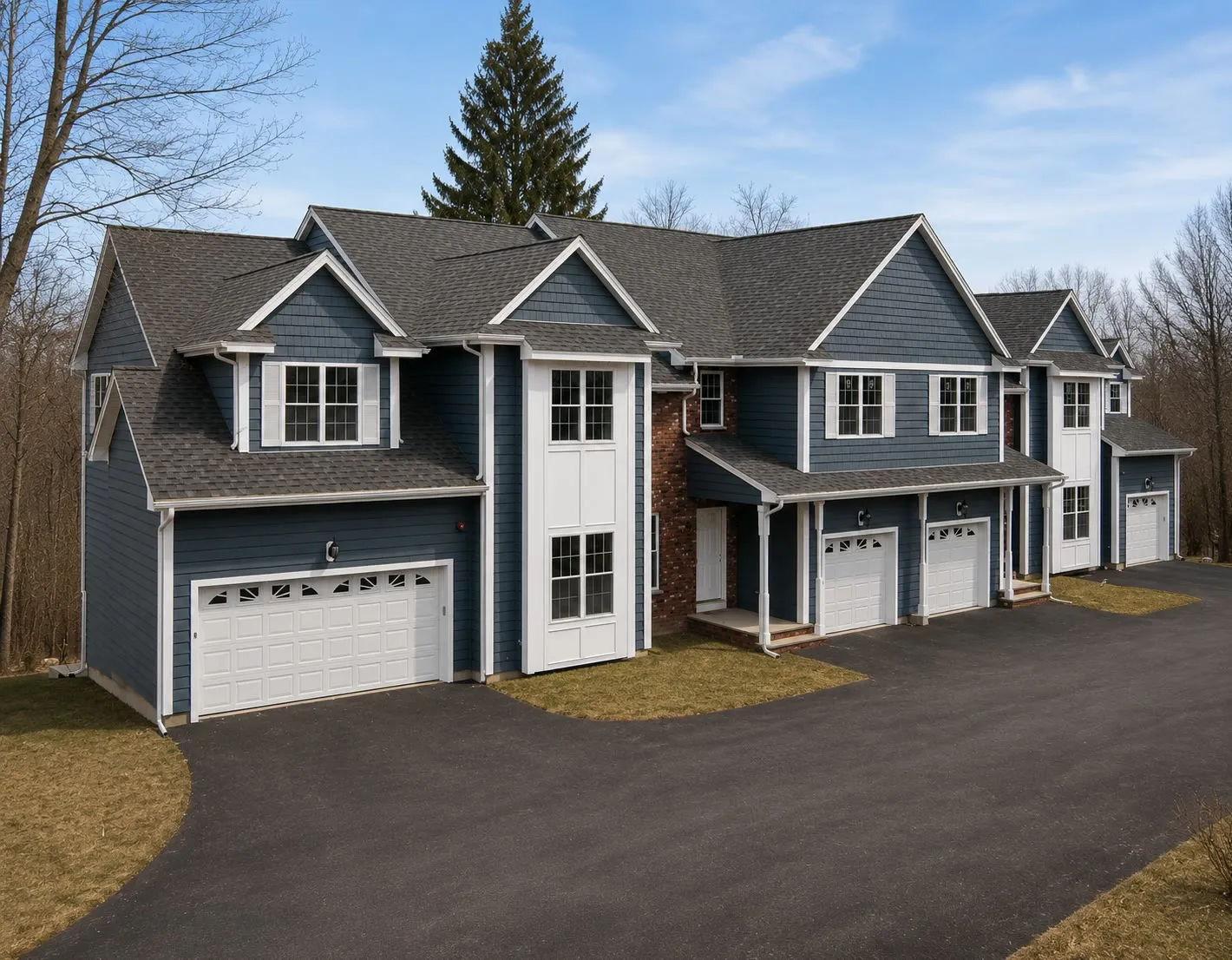 Row of blue-gray attached townhouses with shake-sided gables, white trim, and white garage doors along a new driveway