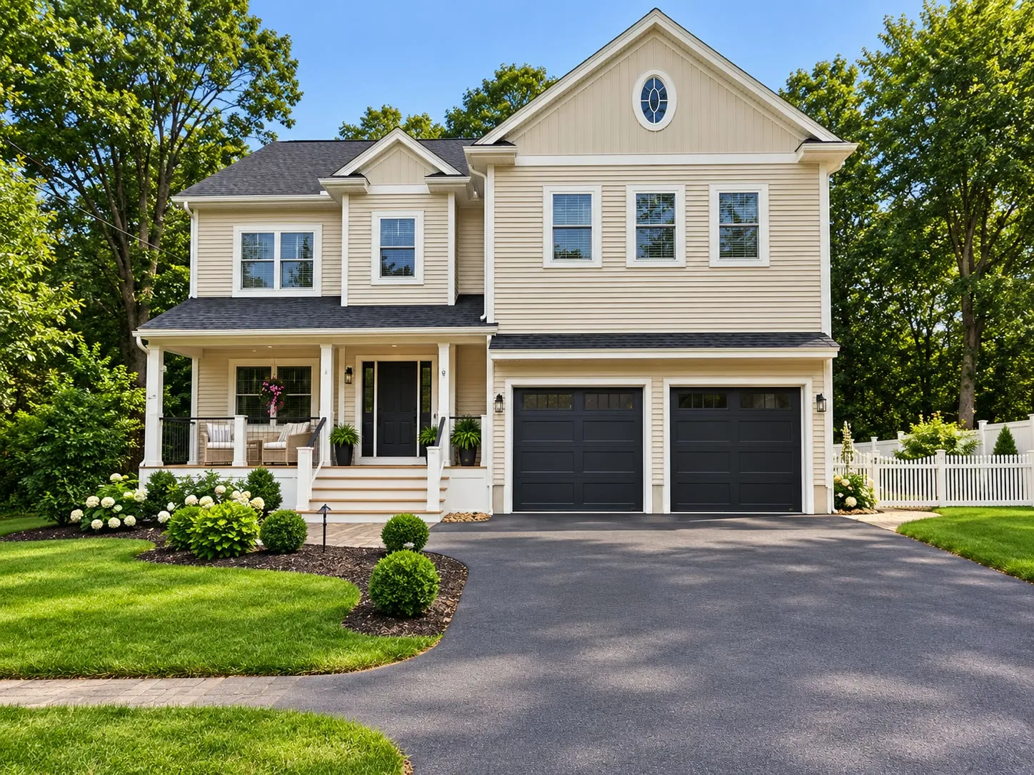 Cream two-story home with an oval attic window, a farmer’s porch, black shutters, and a dark garage door