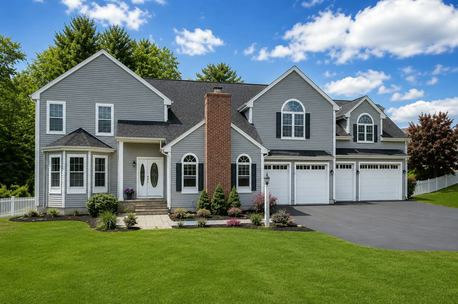 Gray colonial with a brick chimney, arched windows, a bay window, and a three-car garage with white doors