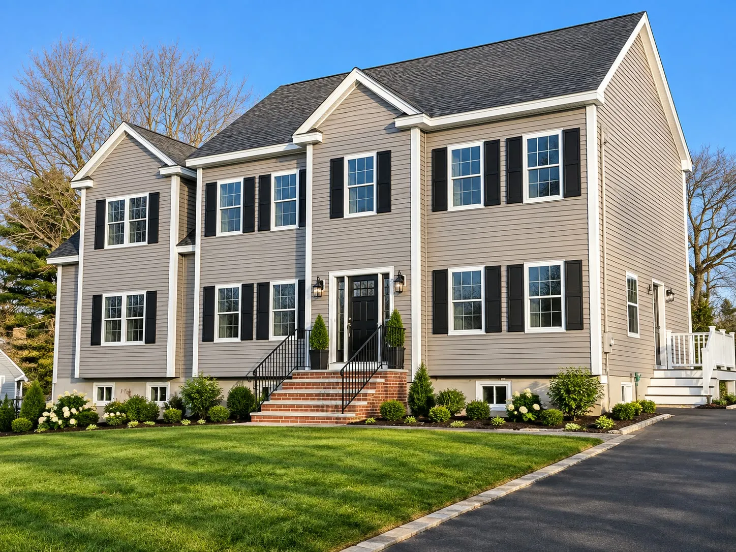 Tan two-story colonial with black shutters, twin front gables, iron stair railings, and brick steps