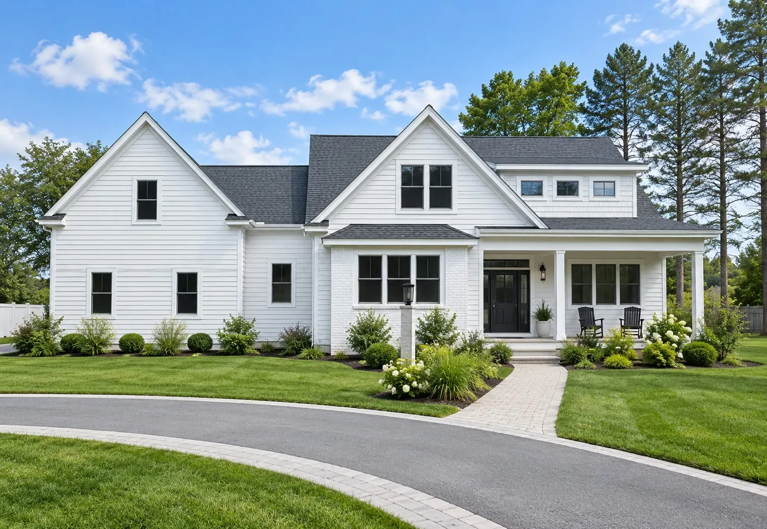 White farmhouse with black windows, multiple gables, a covered porch, and a circular paver driveway