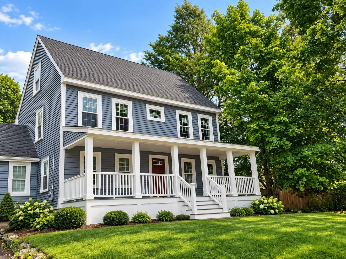 Blue-gray colonial with a full-width white farmer’s porch, a red front door, and an attached single-story wing on the left