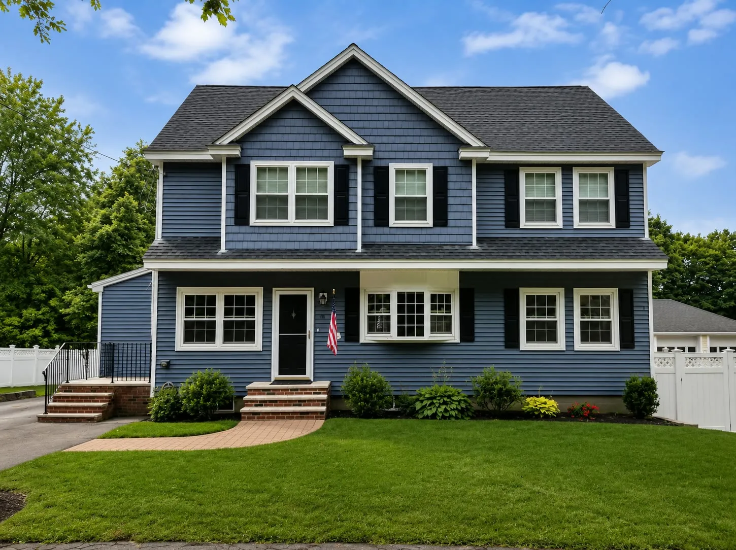 Blue-gray two-story home with two front gables, shake-sided gable ends, a bay window, black shutters, and brick steps to the entry