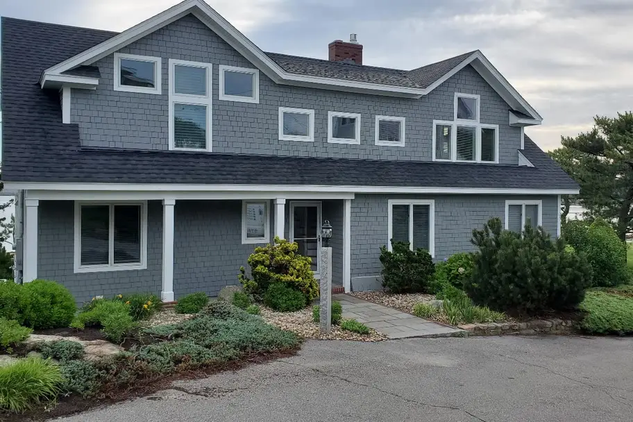 Gray cedar-shingle two-story waterfront home with a row of dormer windows and a covered front porch