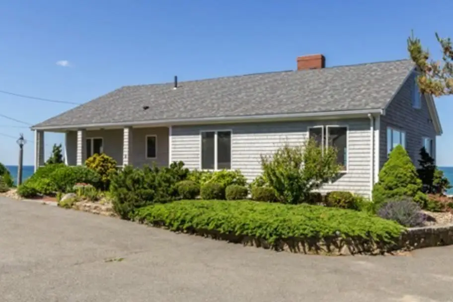 Gray cedar-shingle single-story waterfront home with a covered porch and ocean behind